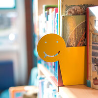 Ein aus Pappe gefertigter smiley zwischen Büchern in der Stadtbücherei Hürth.