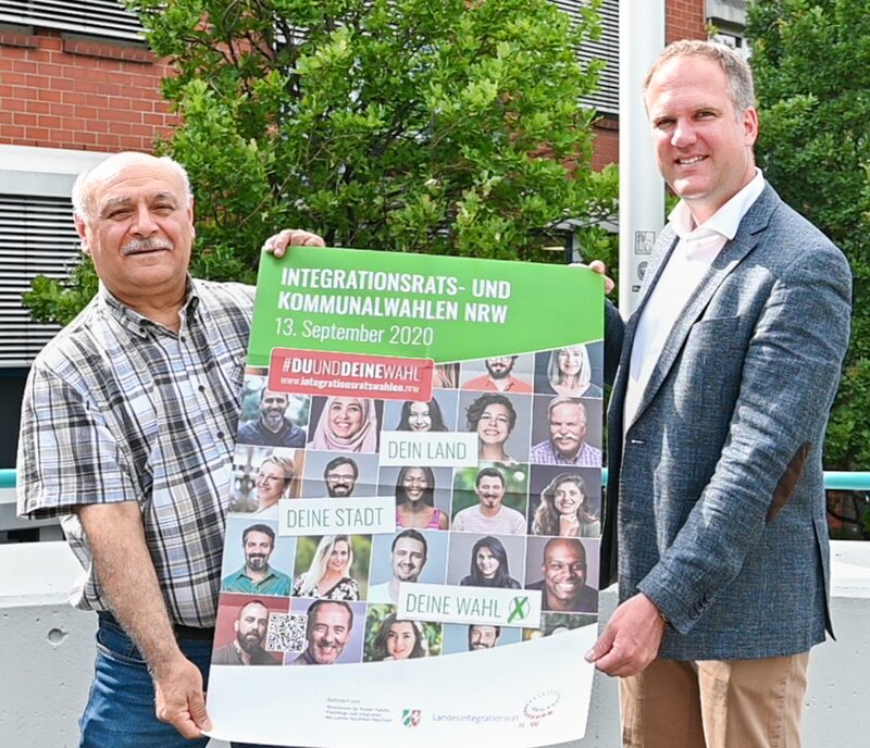 Bürgermeister Dirk Breuer und Bektas Metin, Vorsitzender des Integrationsrates der Stadt Hürth, halten ein Plakat zur Integrationsrats- und kommunalwahl NRW..