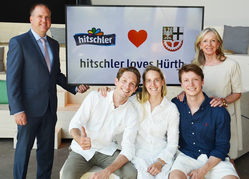 Gabriele Hitschler-Becker, Nicolas Hitschler-Becker, Julia Hitschler-Becker und Philip Hitschler-Becker und Bürgermeister Dirk Breuer stehen vor einem Schild mit dem Slogan „Hitschler loves Hürth“.