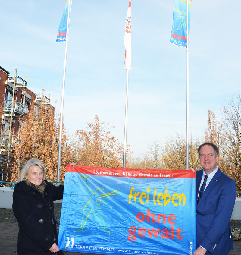 Bürgermeister Dirk Breuer und Gleichstellungsbeauftragte Silke Naumann spannten ein Banner vor den gehissten Fahnen der Organisation „Terre des Femmes e.V.“