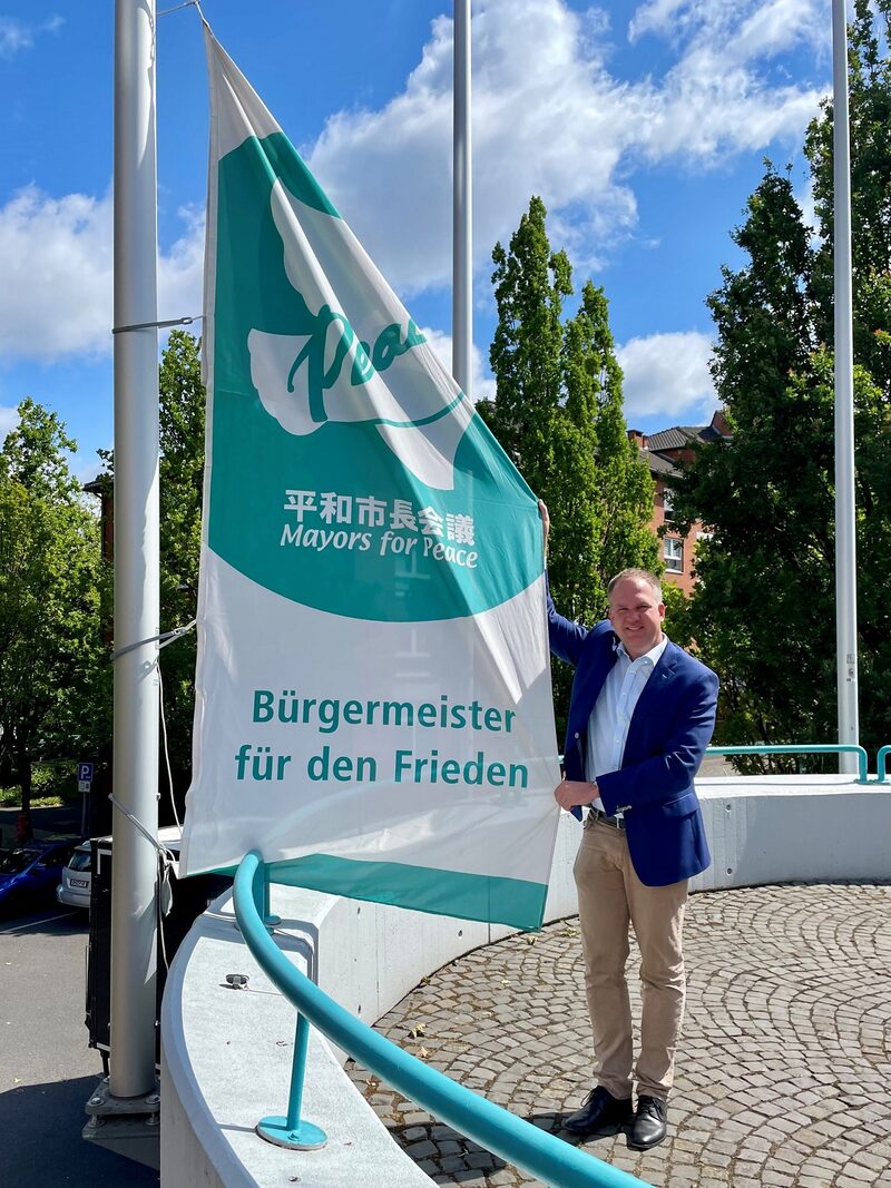 Bürgermeister Dirk Breuer hisst die „Mayors for Peace“-Flagge vor dem Rathaus der Stadt Hürth.
