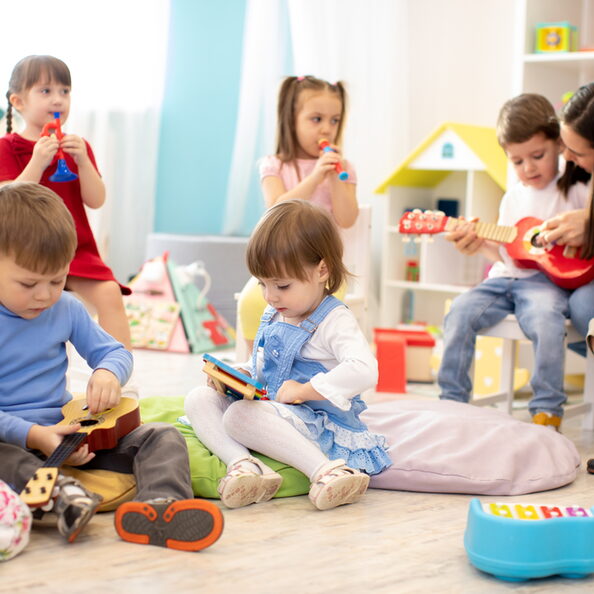 Kindergarten teacher with children on music lesson in day care. Little kids toddlers play together with developmental toys.